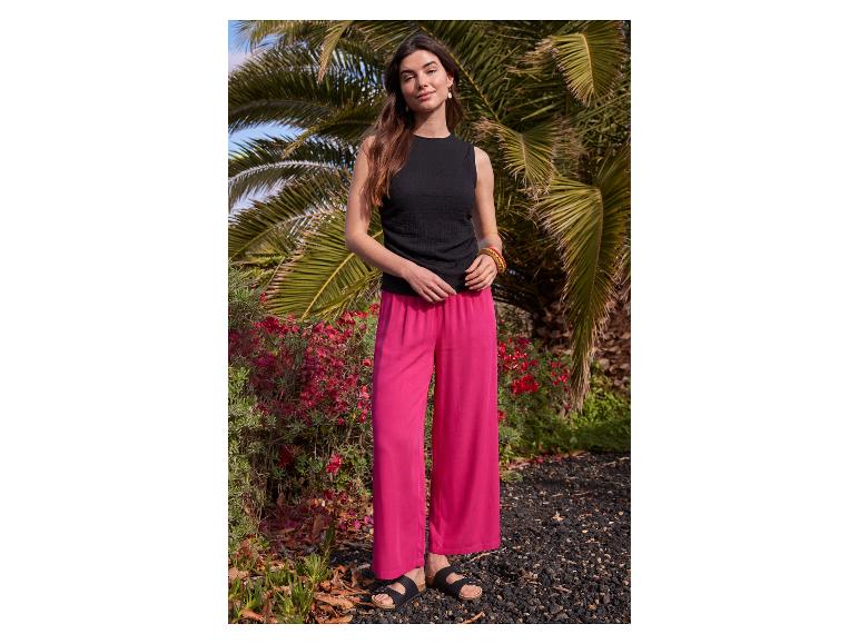 Vrouw in zwarte mouwloze top en felroze wijde broek.