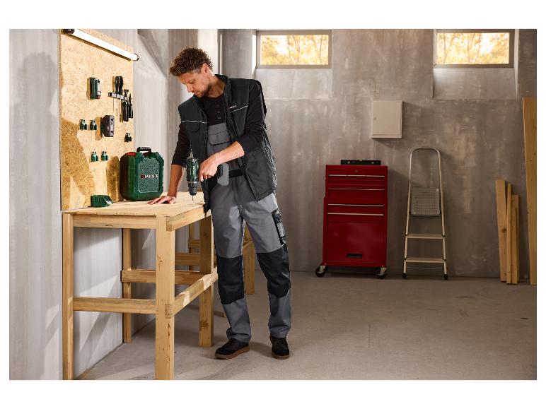 Een man in een PARKSIDE PERFORMANCE® werkgilet boort in een houten tafel in een werkplaats.