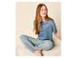 Vrouw in blauw pyjamashirt en gestreepte broek zit op een bank.