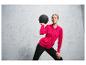 Een vrouw in een roze hoodie en zwarte broek houdt een trainingsbal vast.