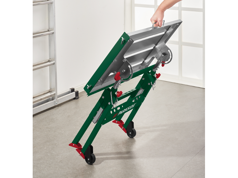 Opvouwbare werkstandaard met wielen, vastgehouden door een hand, met een ladder op de achtergrond.