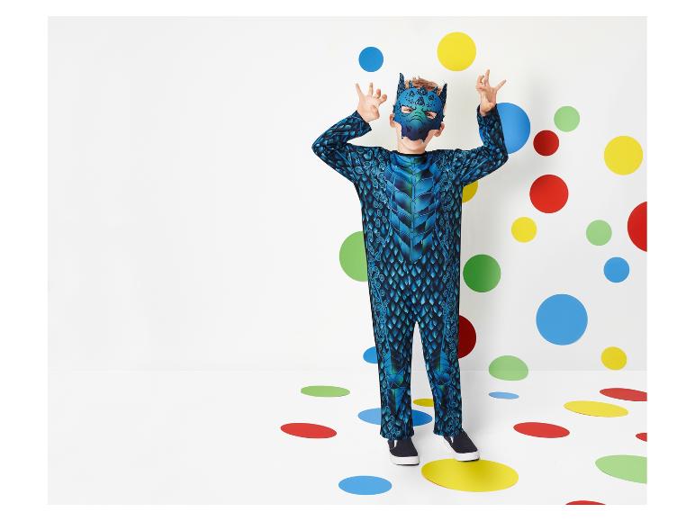 Een jongen in een blauwe drakenkostuum met een drakenmasker voor een witte achtergrond met gekleurde stippen.