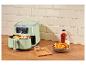 Lichtgroene airfryer met frietjes, ketchup en zout op een houten aanrecht.