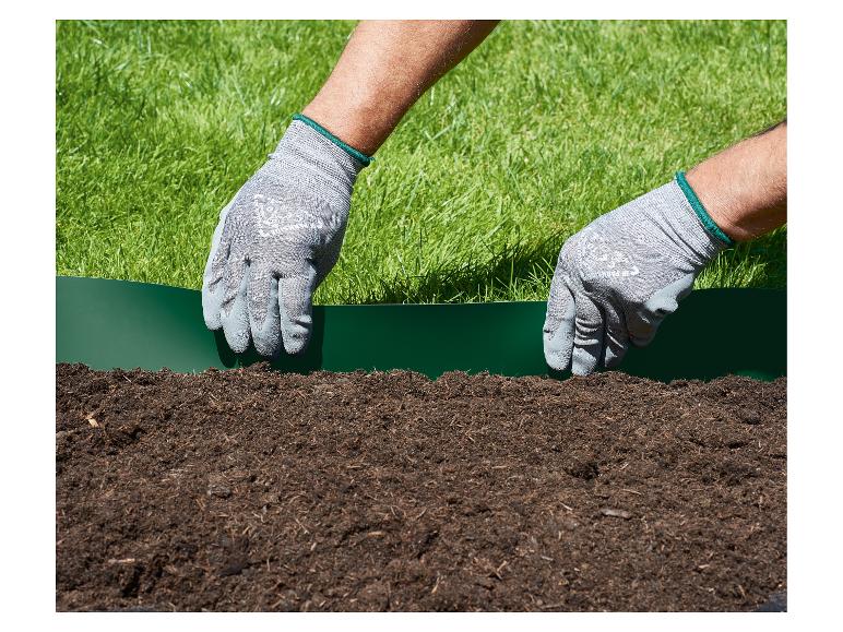 Handen in tuinhandschoenen plaatsen een groene gazonrand tussen gras en aarde.
