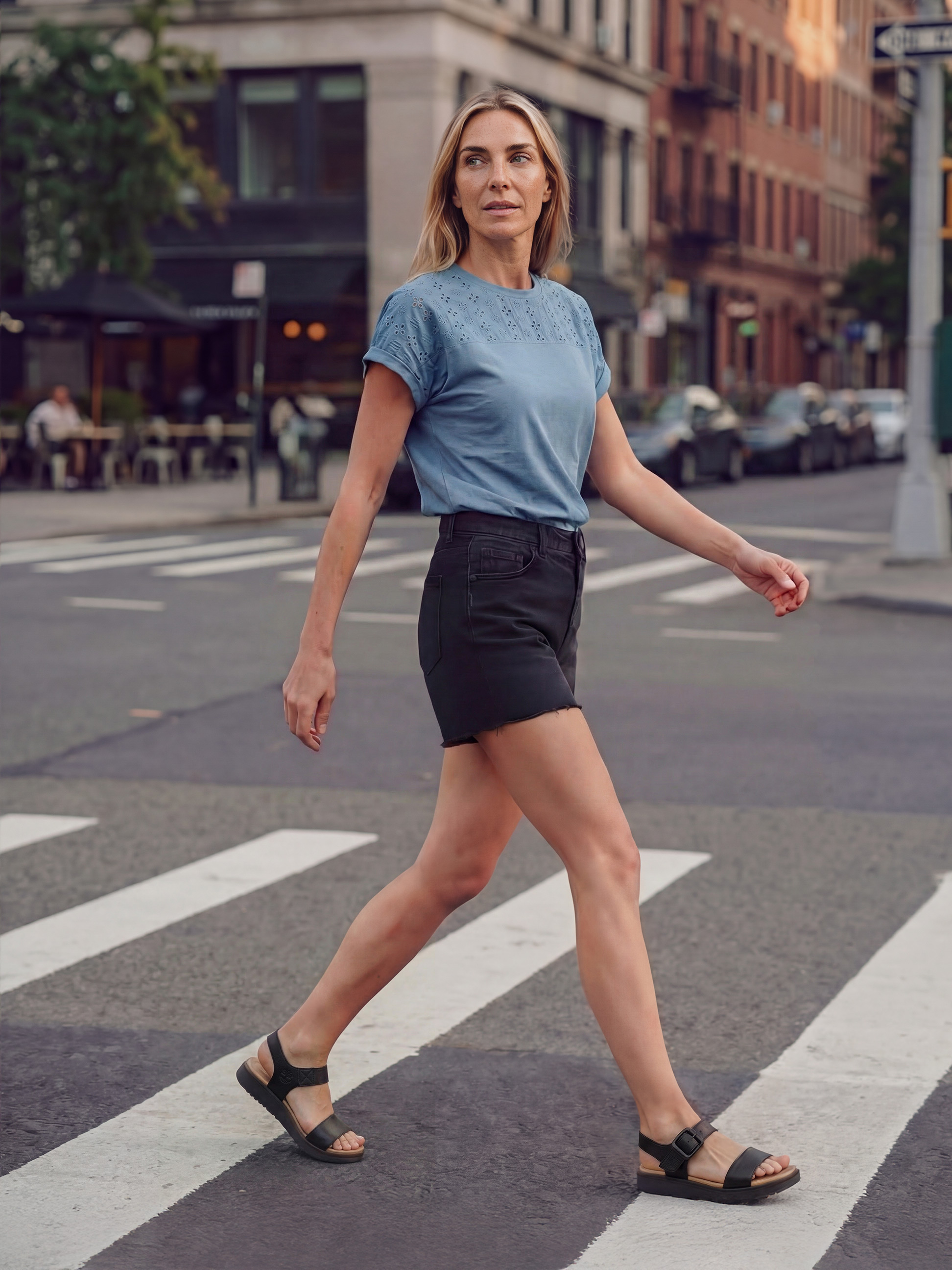 Vrouw in blauw T-shirt en zwarte korte broek steekt de straat over op een zebrapad.