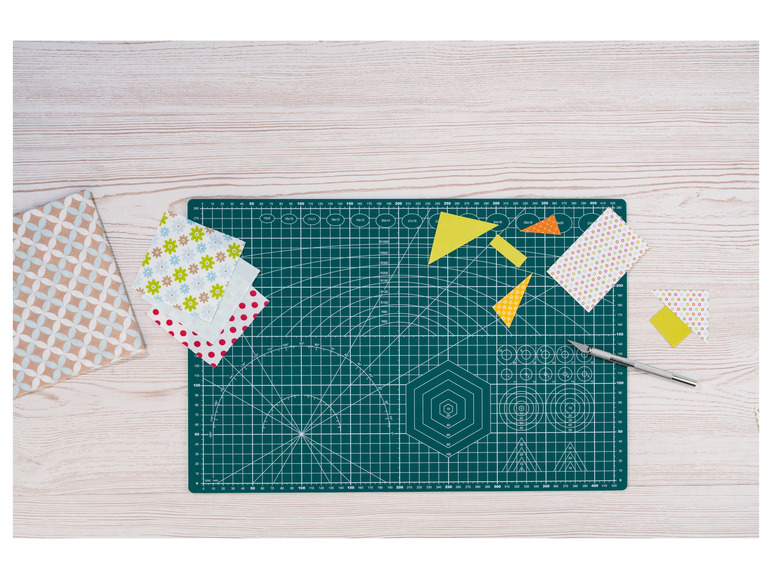 Een groene snijmat met patroonpapier, een mes en gele driehoeken.