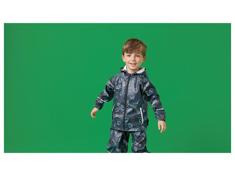 Blije jongen in donkerblauw regenpak met dinosaurusprint.