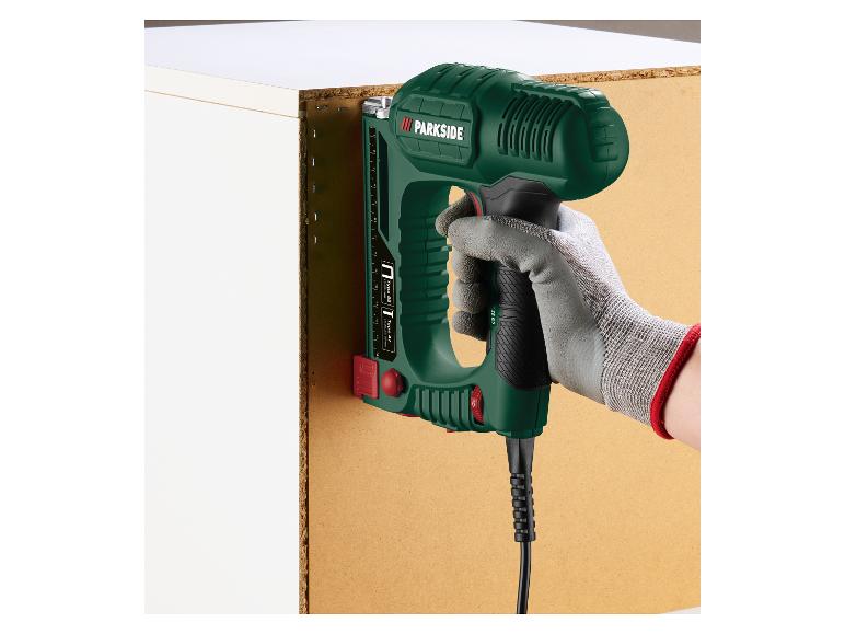 Hand houdt een elektrische tacker vast, waarmee een houten paneel aan een witte kast wordt bevestigd.