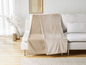Een beige fleece deken en een effen deken op een witte bank.