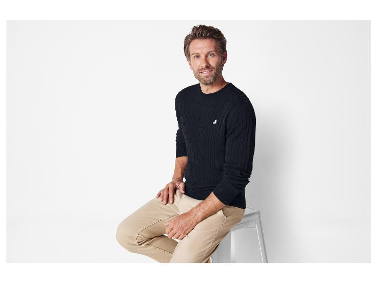 Man in een zwarte trui met kabelbreisel en beige broek.