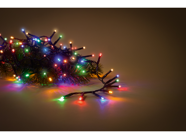 Kleurrijke LED-kerstverlichting verstrengeld met groene dennentakken, die levendige reflecties werpen.