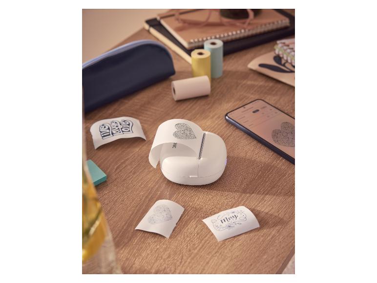 Witte draagbare printer print hartenstickers, op houten tafel met papierrollen.
