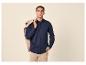 Man in marineblauwe overhemd met knopen en beige broek, beige jas over schouder.