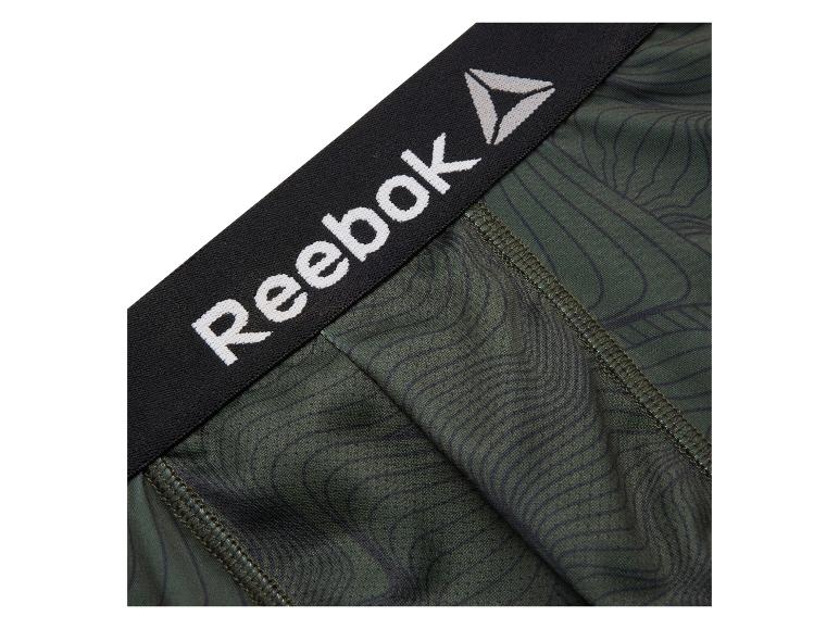 Close-up van groene Reebok compressieshorts met een zwarte tailleband en wit logo.