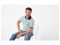 Man in lichtblauwe polo T-shirt met 'SAILING VOYAGER' opdruk en jeans, zittend op een stoel.
