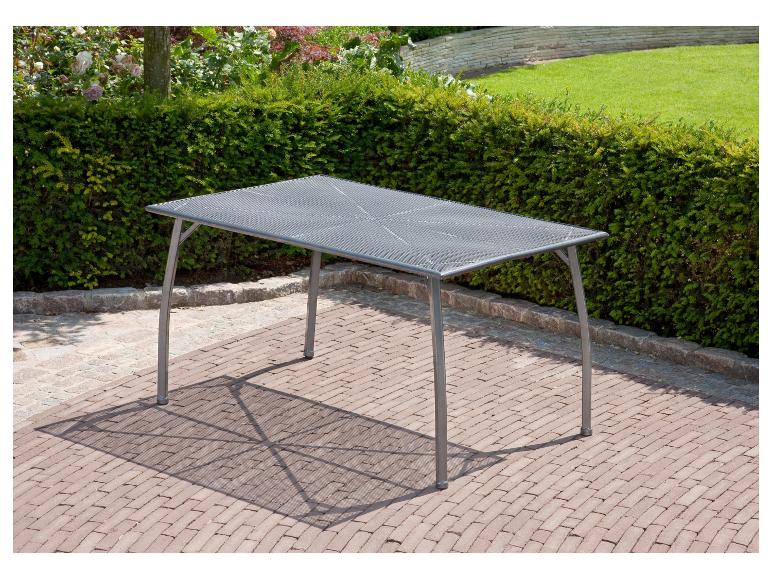Grijze metalen tuintafel op een bakstenen terras met heg en gazon op de achtergrond.