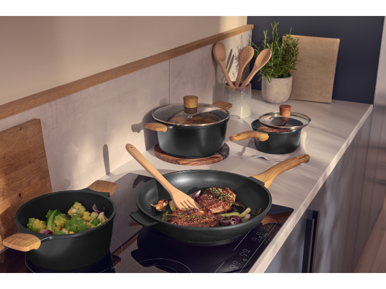 Zwarte potten en pannen met houten handvatten op een inductiekookplaat in de keuken.