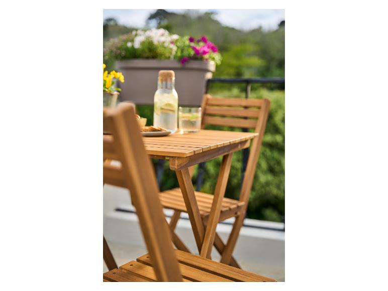 Glazen waterfles en snacks op een houten balkontafel, met bloemen en groen op de achtergrond.