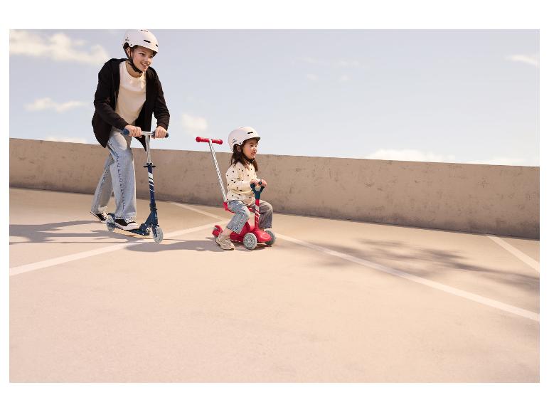 Twee kinderen met helmen rijden buiten op scooters.