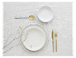 Wit serviesgoed, gouden bestek en minimalistische decoratie.