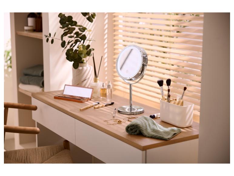 Kaptafel met LED-spiegel, make-upkwasten en cosmetica, met plant en jaloezieën op de achtergrond.