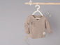 Een beige gebreid shirt met lange mouwen voor baby's, hangend aan een houten hanger.