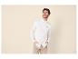 Man in wit overhemd en beige broek, lachend met handen in zakken.