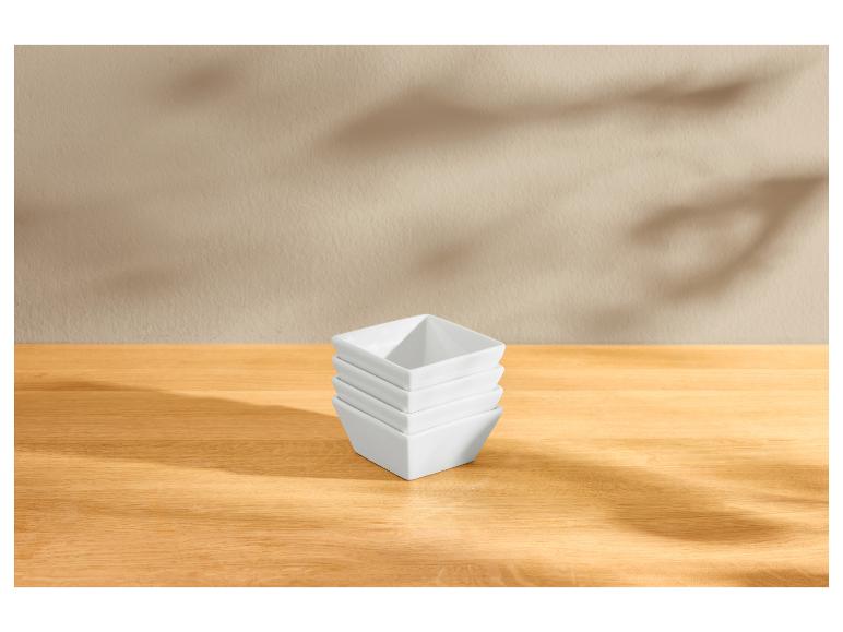 Stapel witte vierkante kommen op een houten tafel met bladschaduwen.