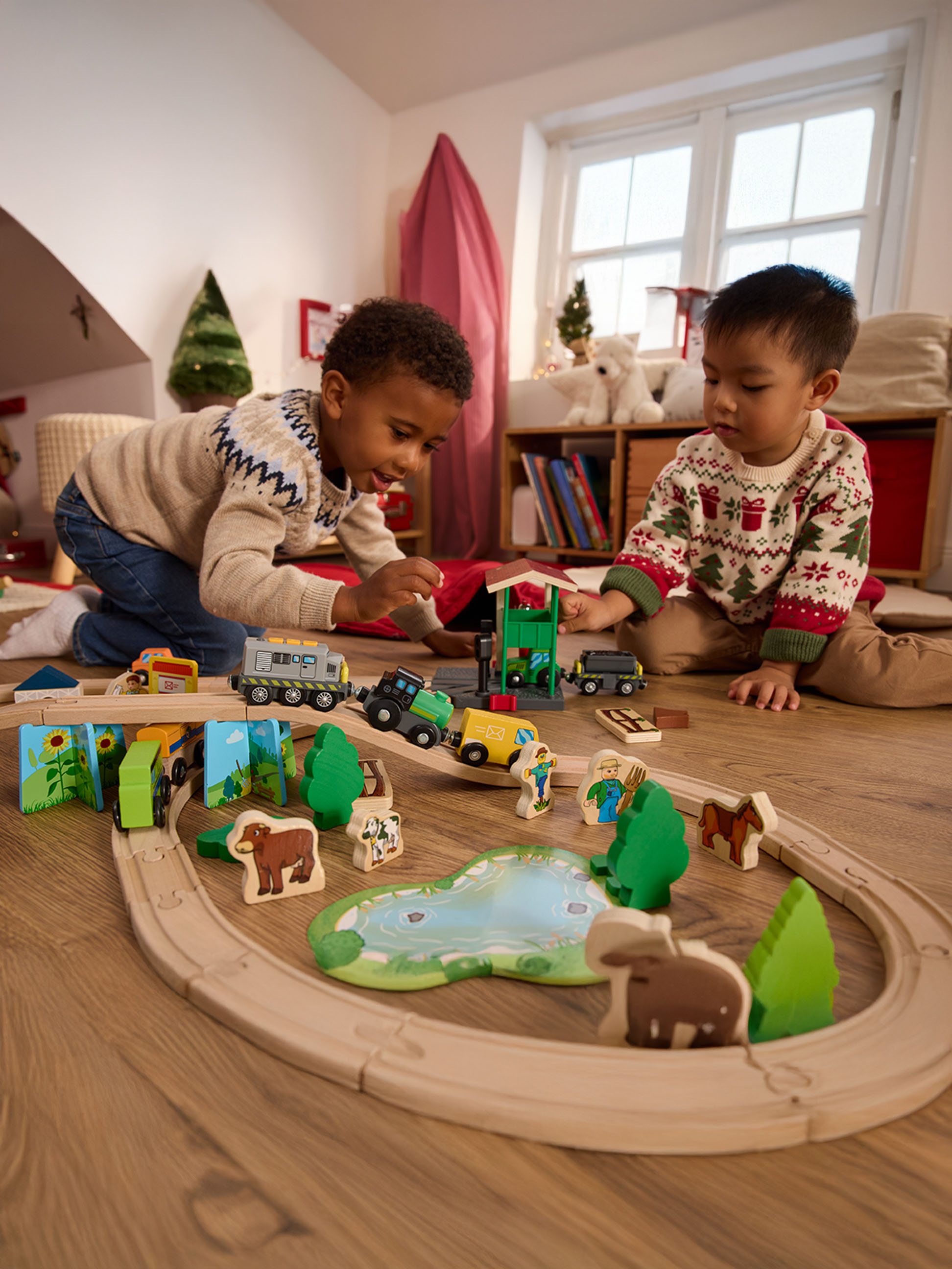 Twee jongens spelen met een houten treinset en boerderijdierfiguren op een houten vloer.