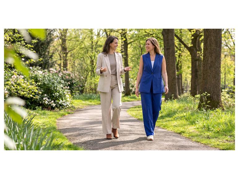 Twee vrouwen in zakelijke casual kleding, een beige en een blauw pak, wandelend in een park.