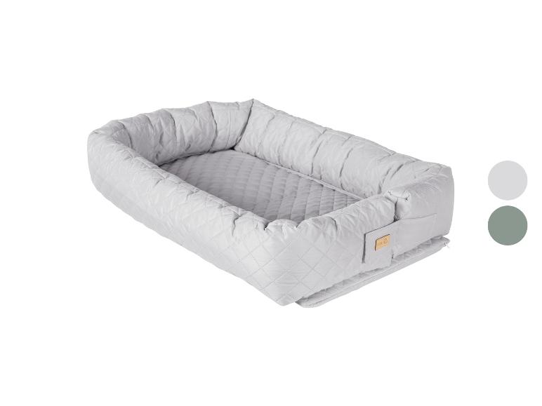 Gewatteerd babynestje in lichtgrijs met een klein houten label, getoond met kleurstalen.