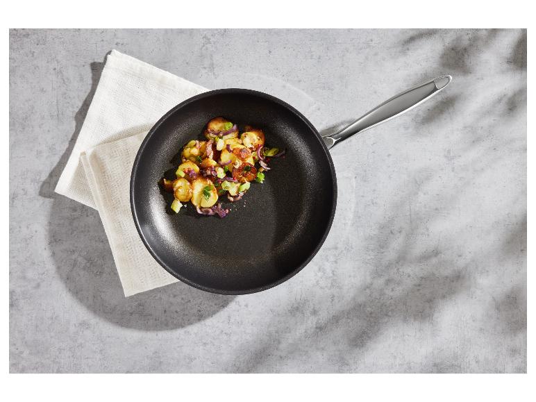 Koekenpan met gebakken aardappelen en groenten op een grijze ondergrond.