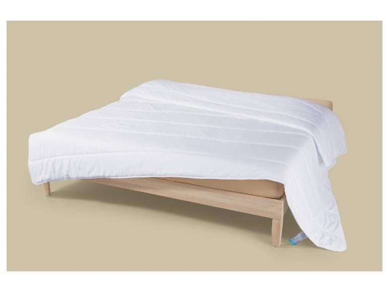 Wit dekbed op een houten bedframe met een beige matras.