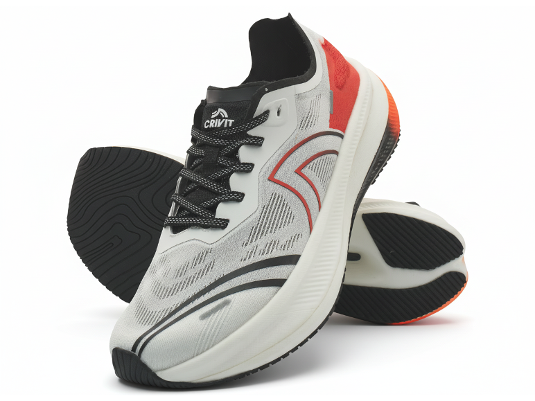 Paar witte en rode sportschoenen met zwarte veters en zolen, één rechtopstaand.