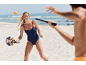 Vrouw in een badpak speelt strandtennis met een racket en bal.