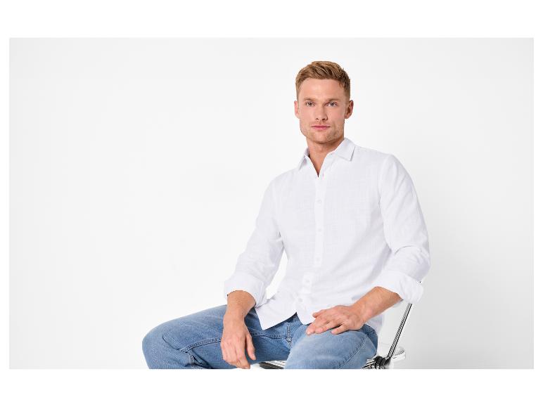 Man in wit overhemd en jeans zittend op een stoel.