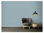 Grijze fauteuil en houten tafel met vaas onder een zwarte lamp tegen een blauwe muur.