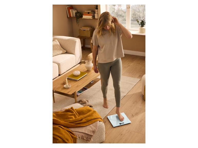 Jonge vrouw in T-shirt en legging, weegt zichzelf op een digitale personenweegschaal.