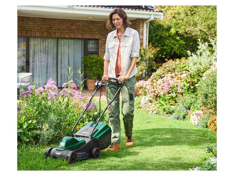 Vrouw maait gras met een Parkside grasmaaier in de tuin van een huis.