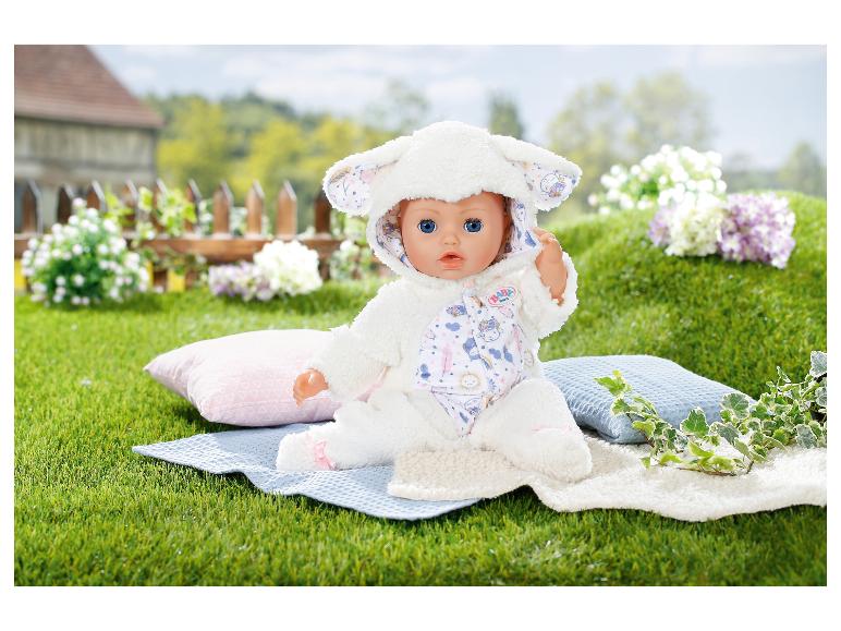 BABY born pop in een lamspak op een deken in het gras met kussens en bloemen.