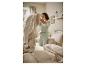 Vrouw in lichtgroene pyjama maakt een bed op met lichtbeige beddengoed in een lichte slaapkamer.