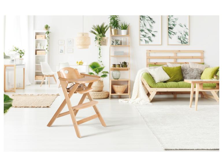 Houten kinderstoel in een lichte woonkamer met groene bank en planten.