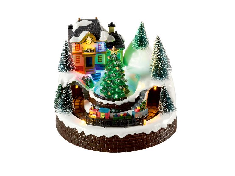 Verlichte kerstscène met een trein, station en besneeuwde bomen.