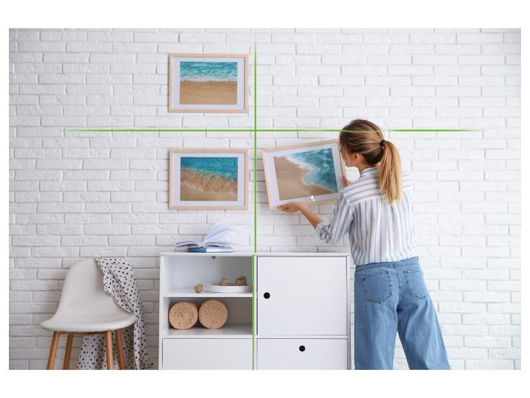 Vrouw hangt schilderijen op boven een wit meubel in een kamer.