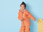 Een meisje draagt een oranje regenjas en broek.