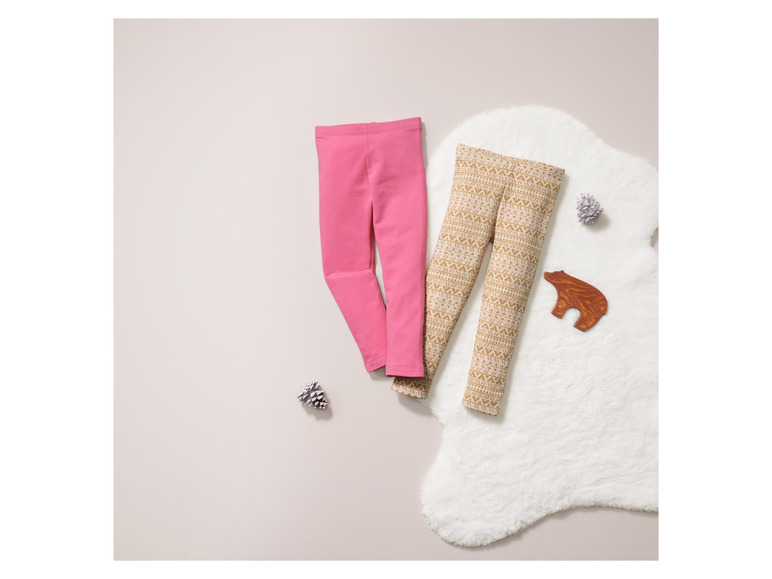 Roze en gepatroneerde leggings voor kinderen op een witte vacht.