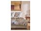 Bed met beige bloemendekbedovertrek en kussens, houten nachtkastje met lamp en decoratie.