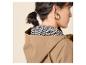 Vrouw in beige jas met capuchon en zwart-wit patroonblouse, gouden oorbellen.