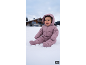 Lachende baby in een roze sneeuwpak zittend in de sneeuw met een huis op de achtergrond.