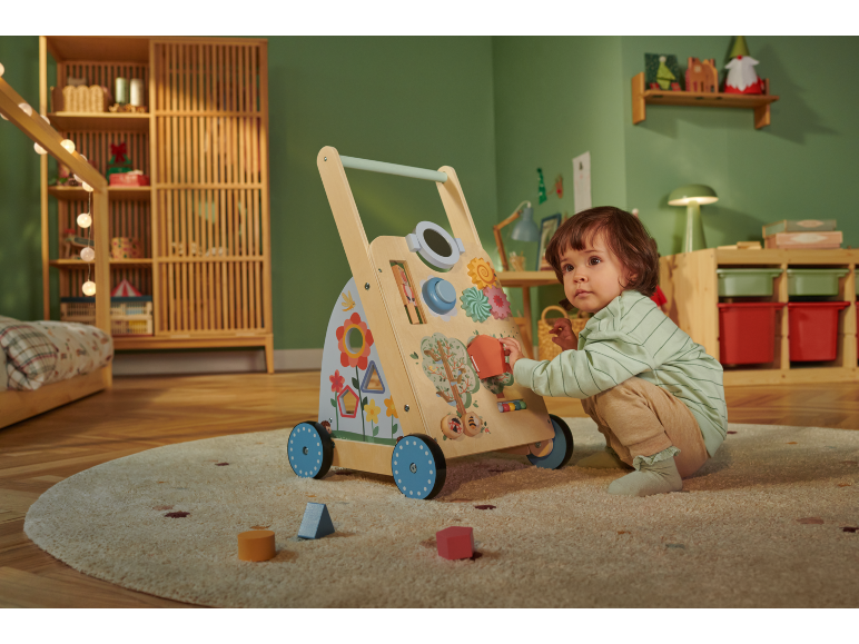 Peuter speelt met een multifunctionele houten loopwagen in een groene kinderkamer.